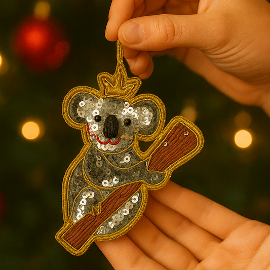 Hand holding a sequined koala ornament with a blurred Christmas tree background