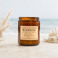 An amber glass jar candle labeled 'BEACH DAYS' by Harney & Co. Sydney, styled on a light stone surface with blurred seashells and a beach background.