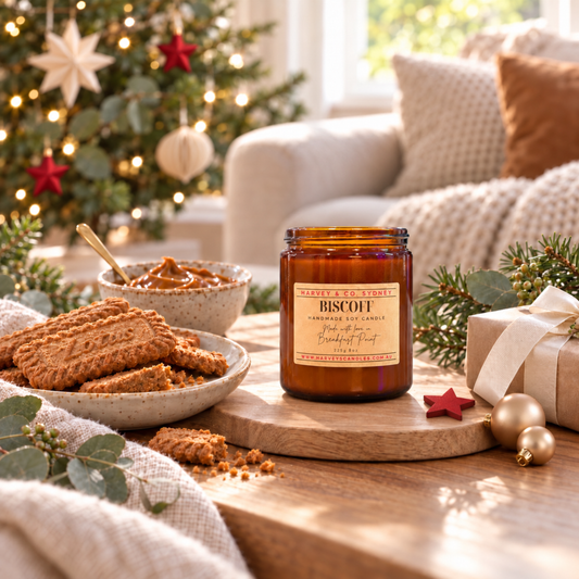 Harvey & Co. Sydney Biscoff candle in an amber jar beside caramelised biscuits, with red star decorations and a softly lit Christmas tree.