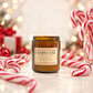 An amber glass jar candle labeled 'CANDY CANE' by Harvey & Co Sydney sits on a light surface with red-and-white candy canes and festive blurred lights in the background.