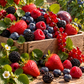 A wooden crate overflowing with fresh red strawberries, blueberries, blackberries, and red currants in a sunny berry field.