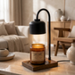 Black table lamp with a white candle on a wooden base next to a potted plant and bowls.