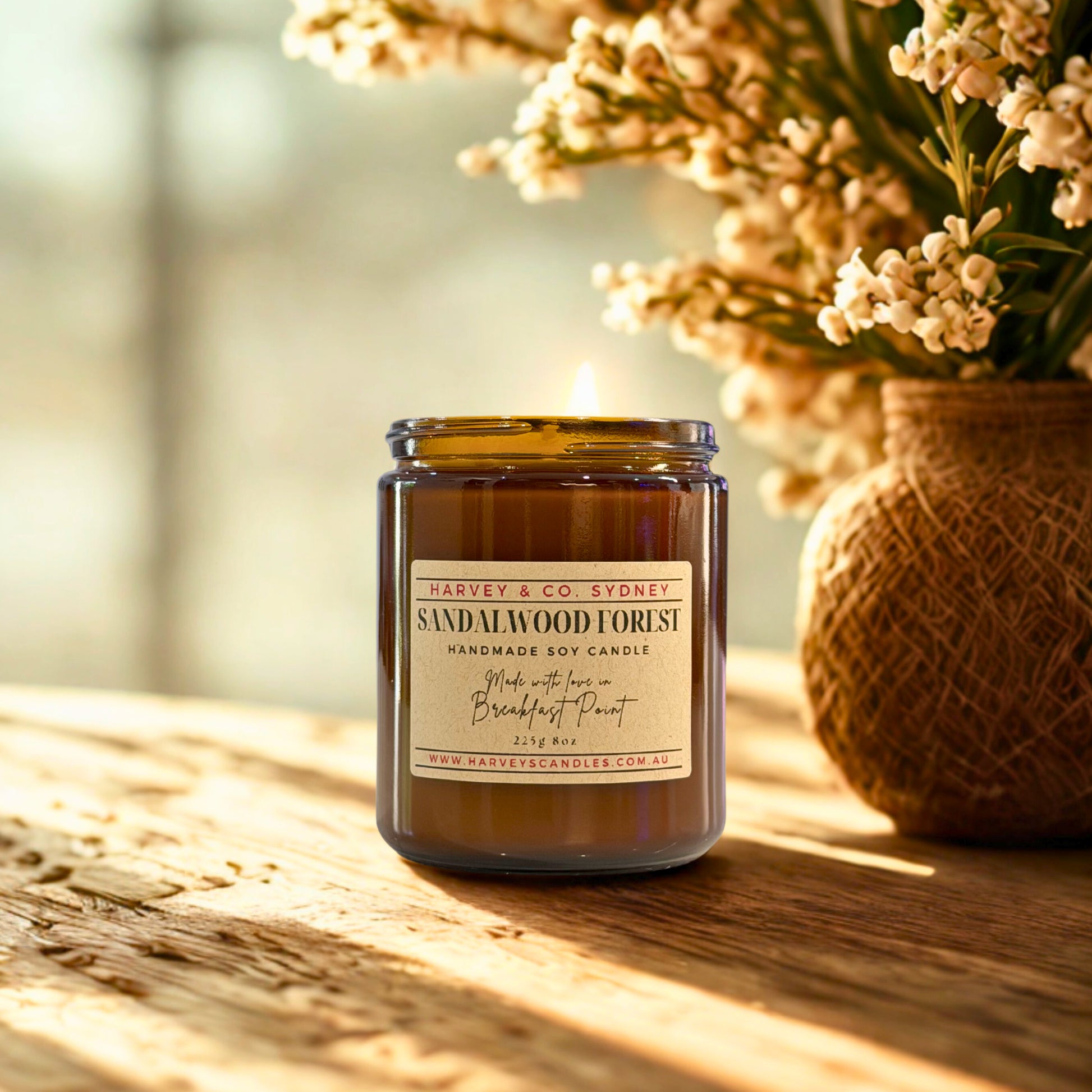 Harvey & Co. Sydney sandalwood forest candle on a wooden surface with a vase of flowers in the background.
