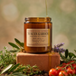 Jar of Tuscan Garden candle with honey being drizzled over it, surrounded by herbs and tomatoes.
