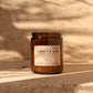 An amber glass jar candle labeled 'GARDEN WALKS' by Harvey & Co. Sydney, placed on a stone surface with warm sunlight and leaf shadows across the scene.