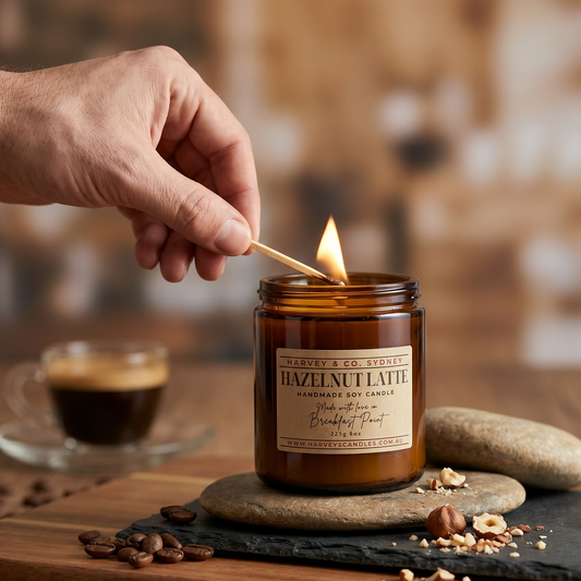 Hand lighting a Hazelnut Latte candle with coffee beans and hazelnuts on a wooden surface.