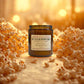 Butter popcorn candle with a label surrounded by popcorn kernels on a warm, blurred background