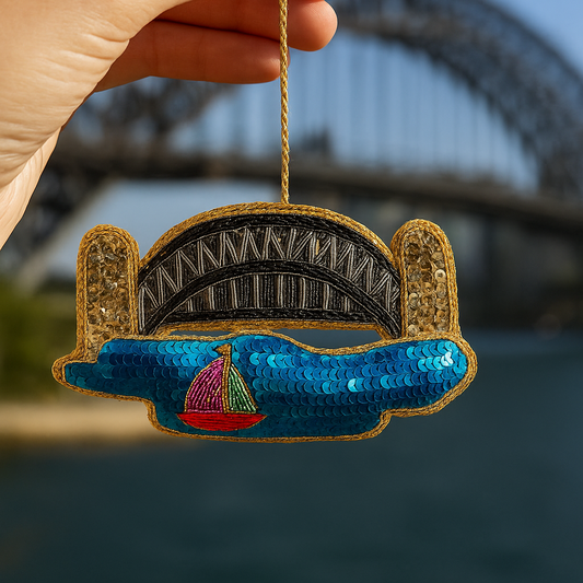 Decorative ornament of a bridge with a sailboat, held against a blurred background.