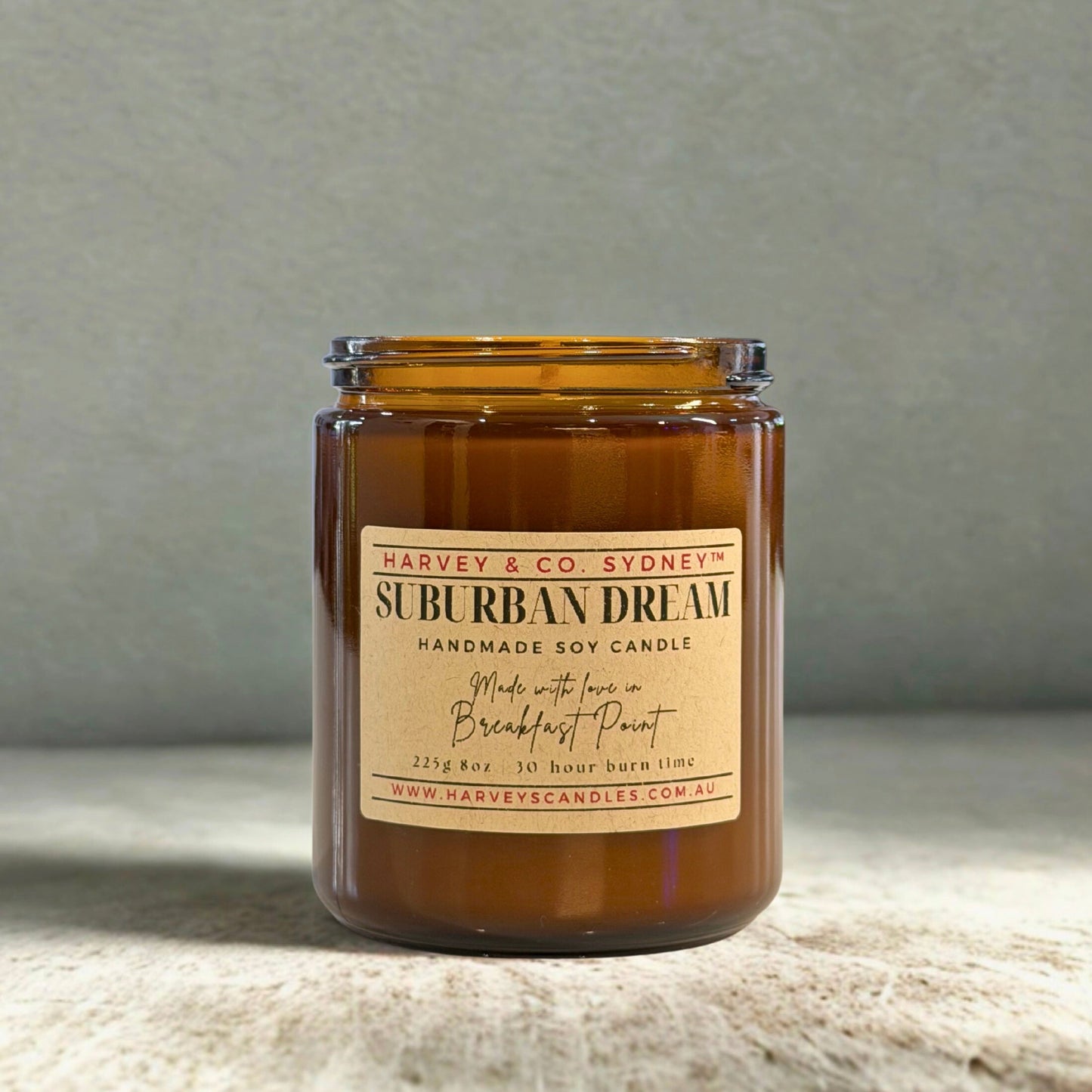 Brown candle in a glass jar with a label on a textured surface and gray background
