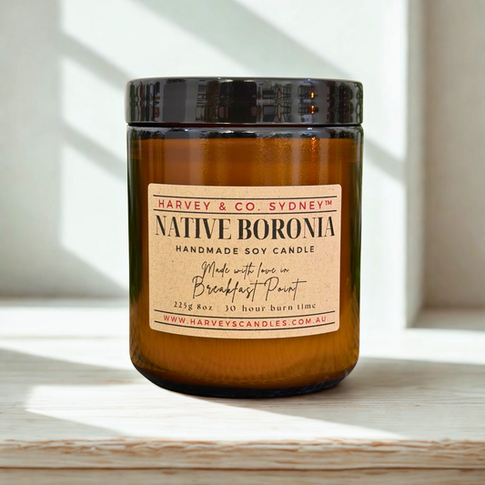 Amber candle with a label on a wooden surface with sunlight filtering through blinds.