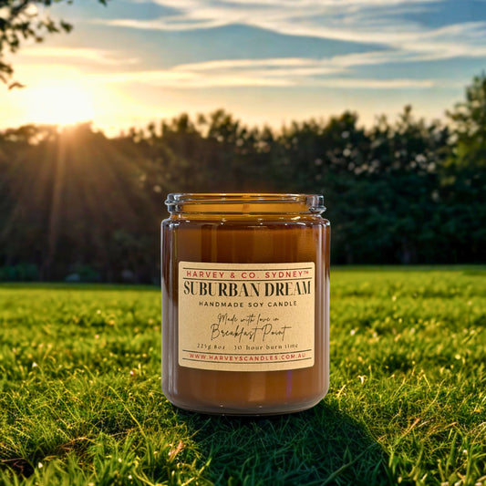 Candle labeled 'Suburban Dream' on grass with sunset background