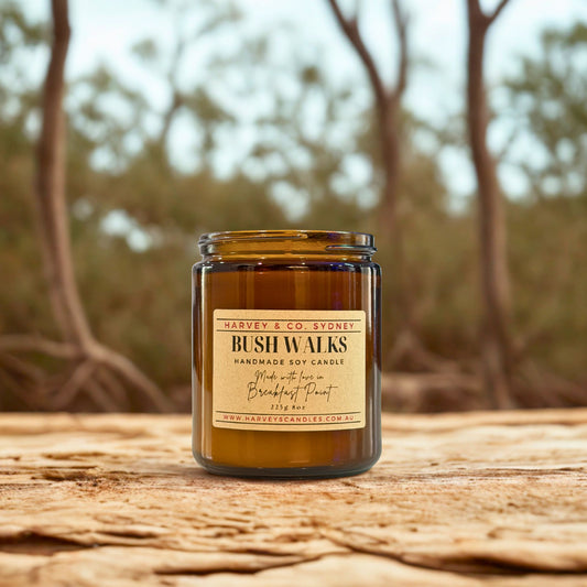 Candle jar labeled 'Bush Walks' by Harvey & Co. Sydney on a wooden surface with a blurred natural background.