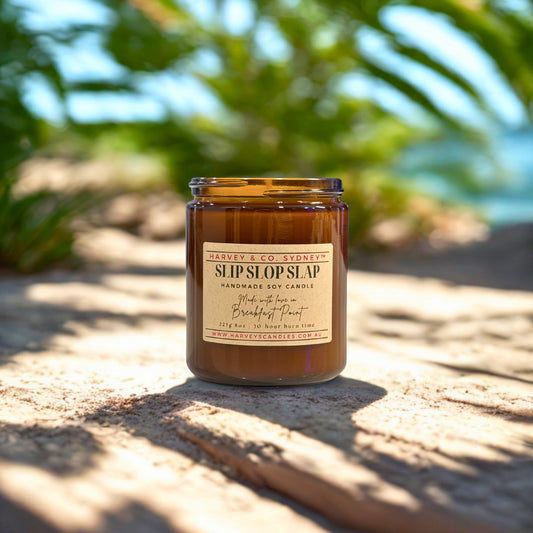 Harvey & Co. Sydney candle labeled 'Slip SlipSlap' on a sandy surface with blurred greenery in the background
