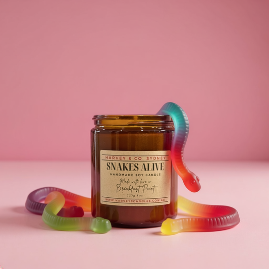Jar of 'Snakes Alive' candle with gummy worm decorations on a pink background