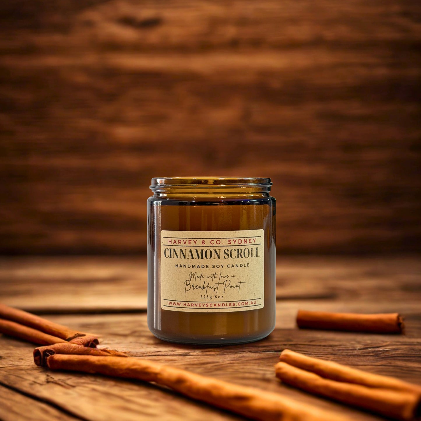 Candle labeled 'Cinnamon Scroll' by Harvey & Co. Sydney on a wooden surface with cinnamon sticks.