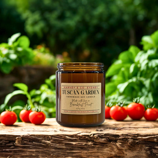 Candle labeled 'Tuscan Garden' by Harvey & Co. Sydney on a wooden surface with tomatoes and greenery in the background.