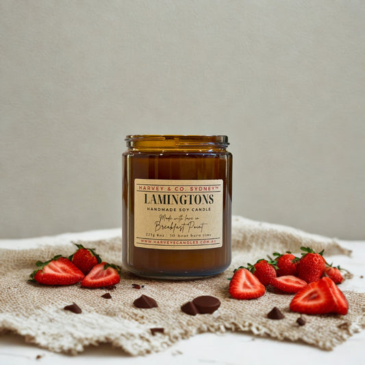 Candle jar labeled 'Lamingtons' surrounded by strawberries and chocolate on a textured surface.