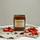Candle jar labeled 'Lamingtons' surrounded by strawberries and chocolate on a textured surface.
