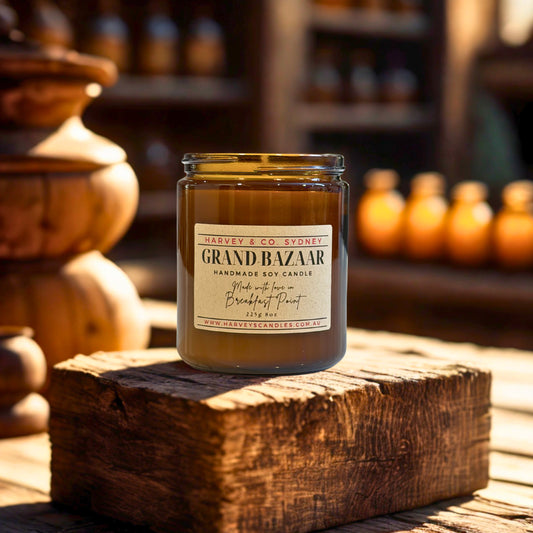 Jar of Grand Bazaar candle on a wooden block with blurred bottles in the background