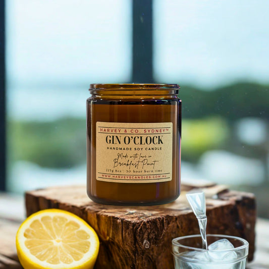 Candle labeled 'Gin O'Clock' by Harvey & Co. Sydney on a wooden block with a lemon and glass of ice.