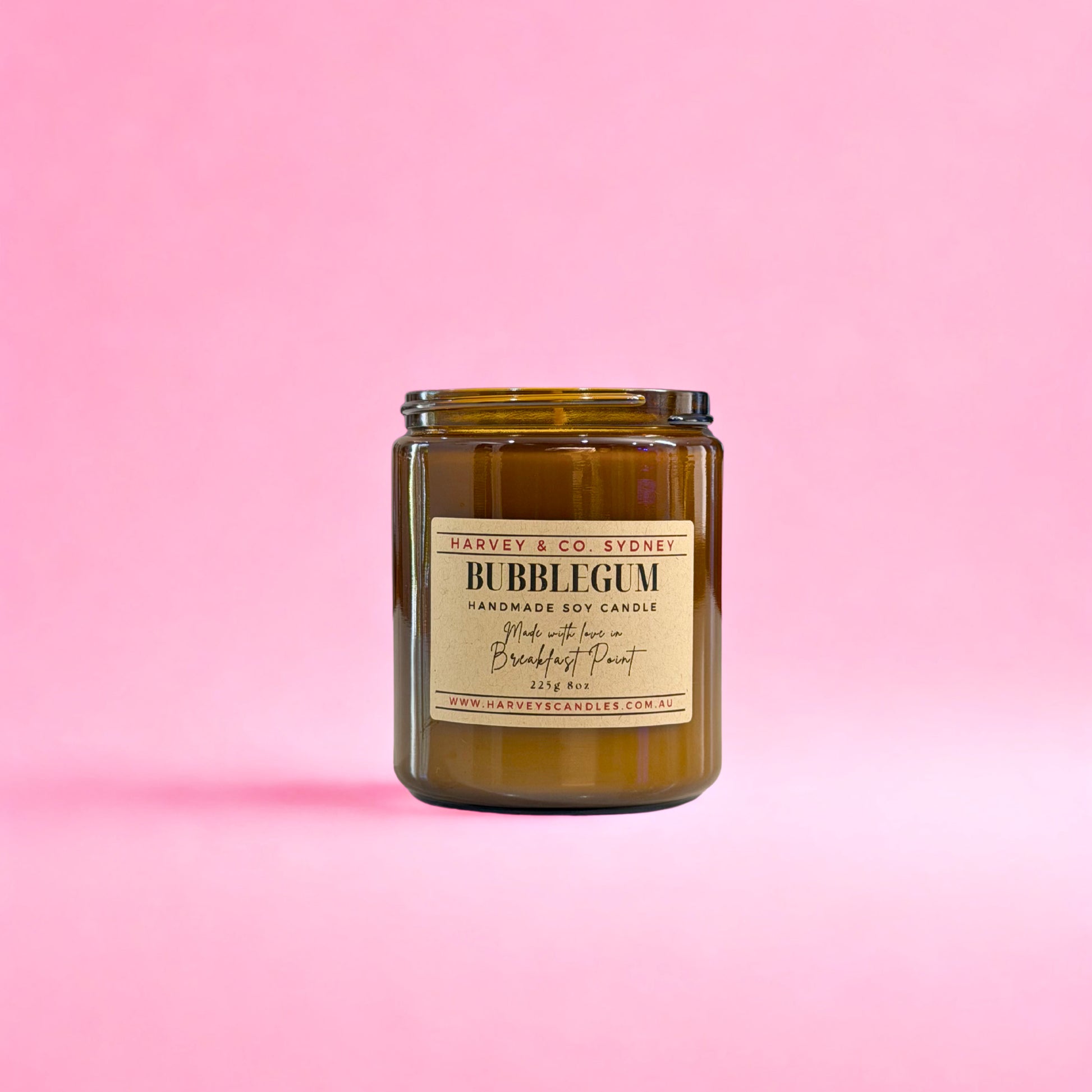 Handmade soy candle in a amber jar with a label on a pink background