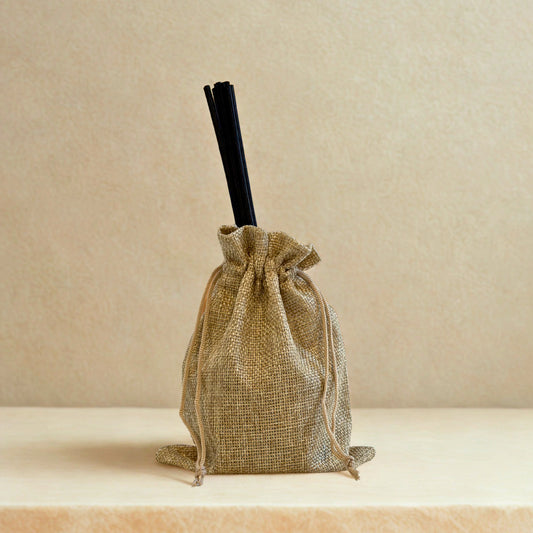 Jute drawstring bag with black straw on a beige background. For illustration purposes only. May vary slightly. 
