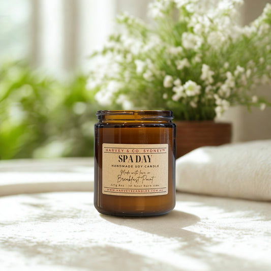 Harvey & Co. Stonethne candle labeled 'Spa Day' on a surface with a blurred background of plants and flowers.