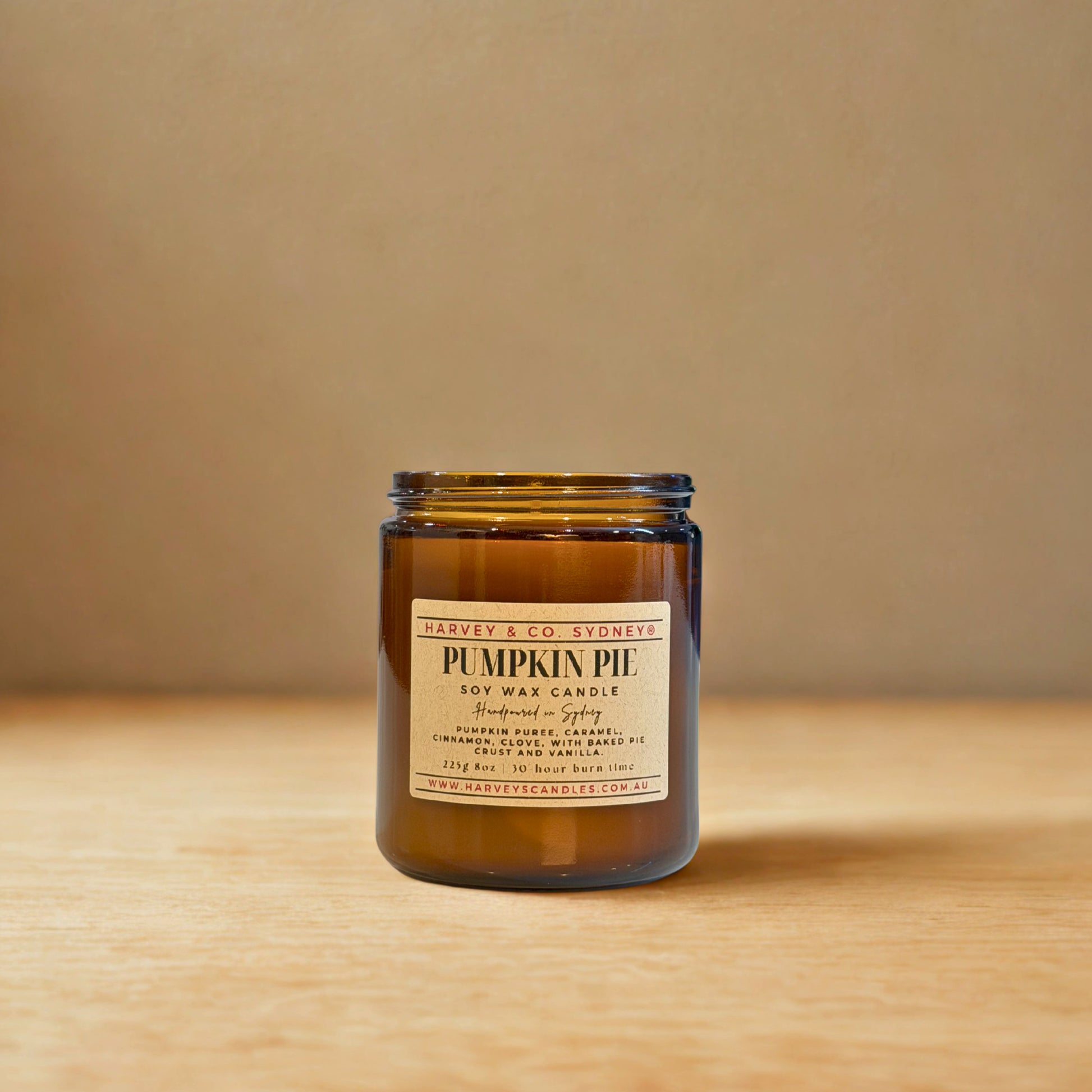 Pumpkin pie candle in a glass jar with a label on a wooden surface and beige background