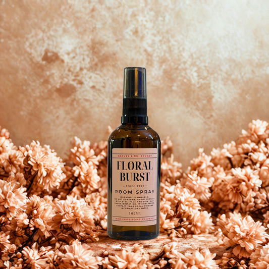 Room spray bottle labeled 'Floral Burst' on a textured surface with flowers.