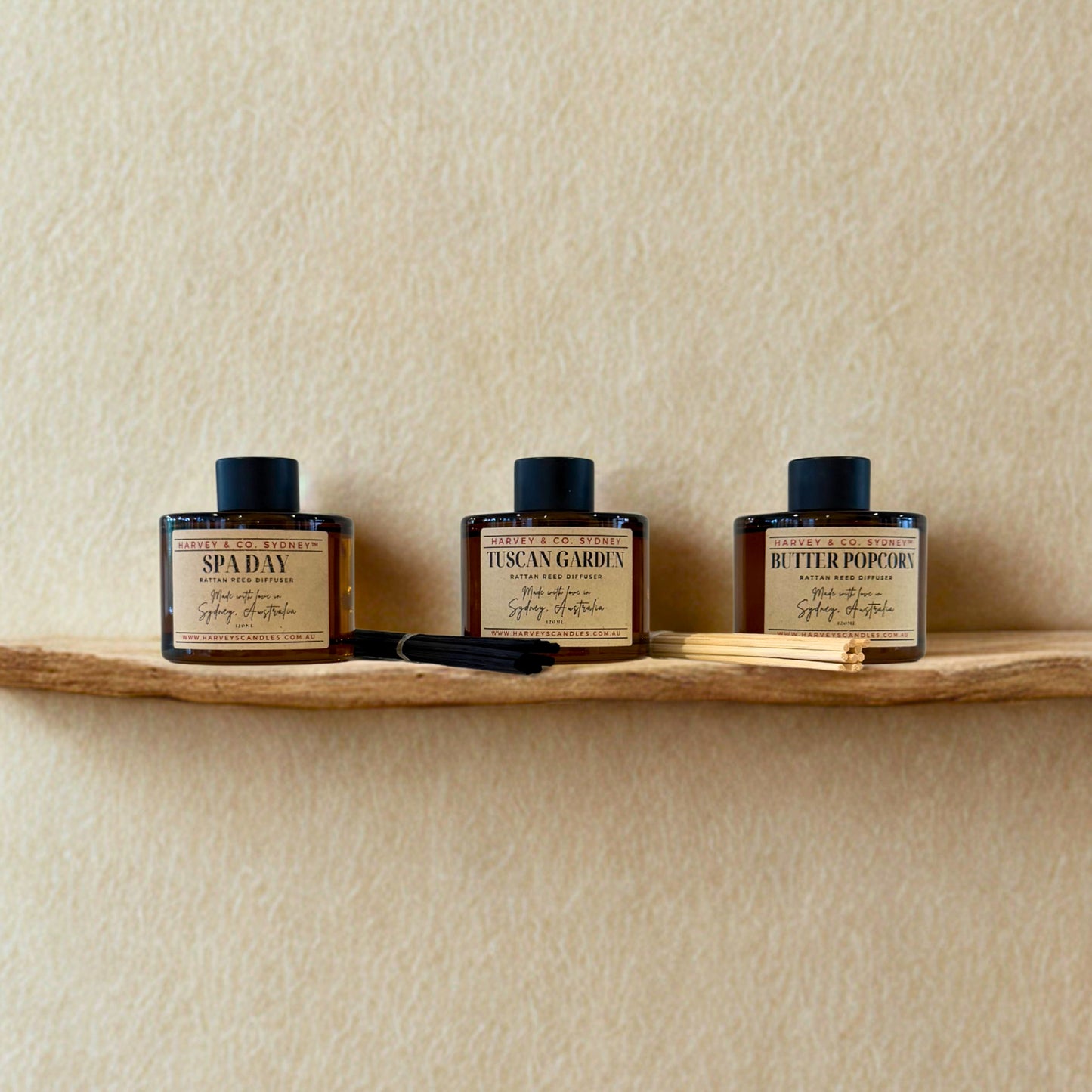 Three rattan reed diffusers on a wooden shelf against a beige wall