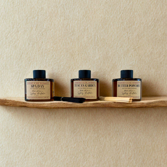Three rattan reed diffusers on a wooden shelf against a beige wall