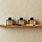 Three rattan reed diffusers on a wooden shelf against a beige wall