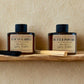 Two diffusers labeled 'Tuscan Garden' and 'Butter Popcorn' on a wooden shelf with a beige background.