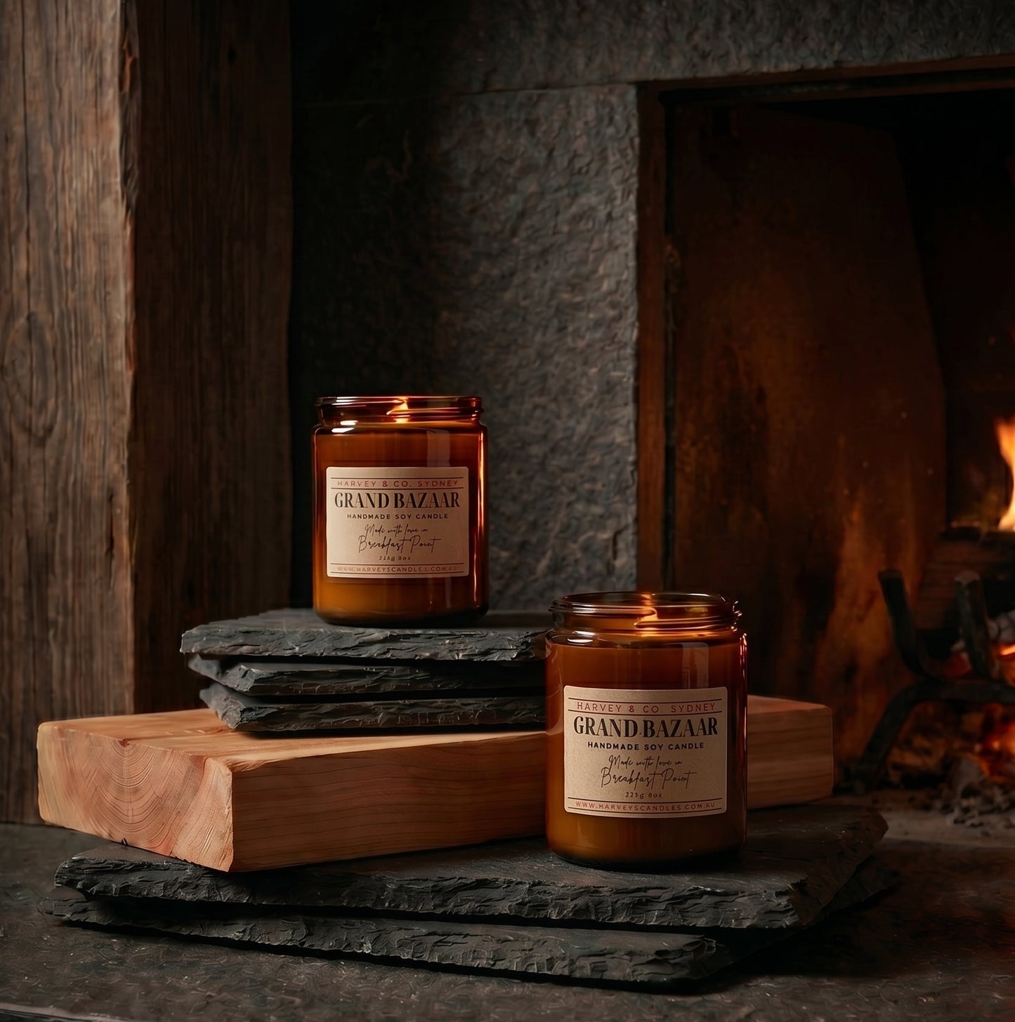 Two candles labeled 'Grand Bazaar' on a wooden cutting board in front of a fireplace.