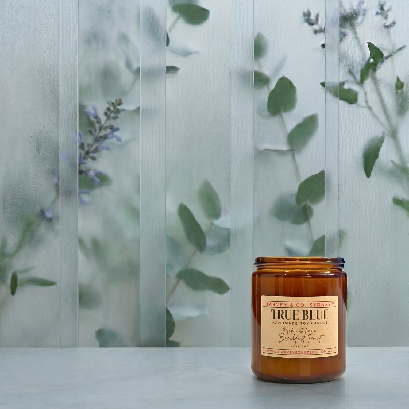 Candle with a label on a surface, with a blurred background of greenery