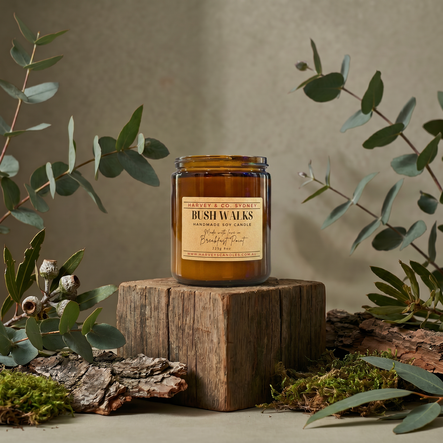 Candle labeled 'Bush Walks' on a wooden block with eucalyptus leaves around
