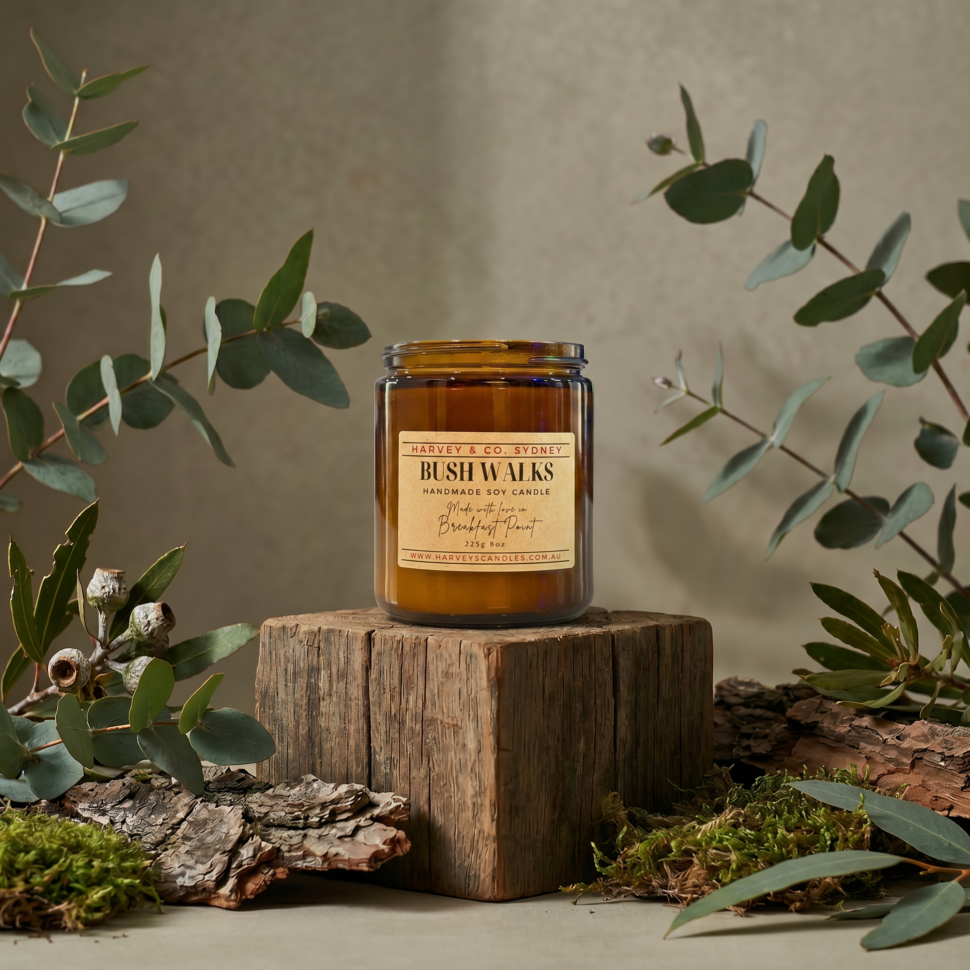 Candle labeled 'Bush Walks' on a wooden block with eucalyptus leaves around