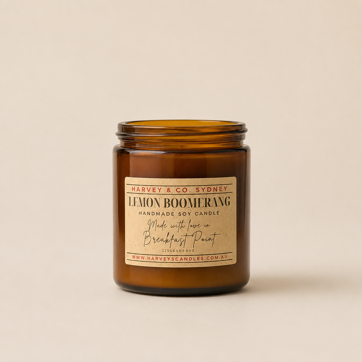 An amber glass jar candle with a cream label reading 'LEMON BOOMERANG' and 'Harvey & Co. Sydney', photographed on a plain warm beige background.