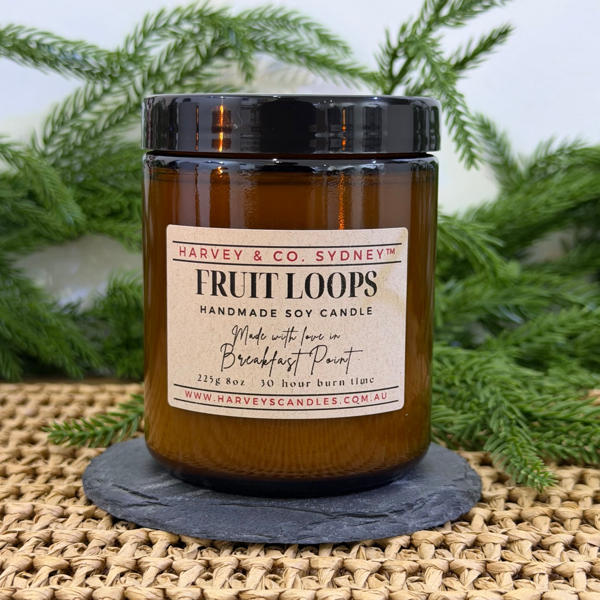 Handmade soy candle labeled 'Fruit Loops' by Harvey & Co. Sydney on a woven surface with greenery in the background.
