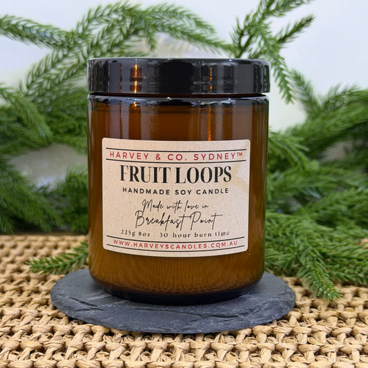 Handmade soy candle labeled 'Fruit Loops' by Harvey & Co. Sydney on a woven surface with greenery in the background.