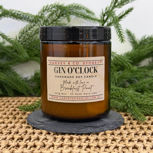 Harvey & Co. Sydney Gin O'Clock candle on a woven surface with greenery in the background