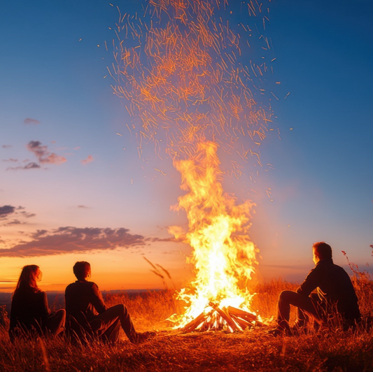 Three people sitting around a bonfire at sunset with a clear sky.