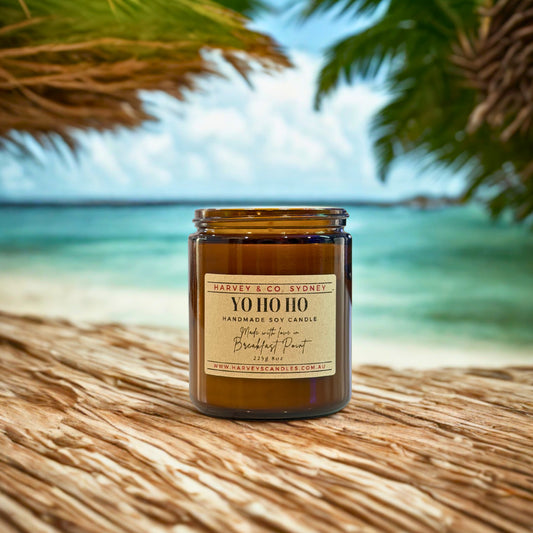 Candle labeled 'YO HO HO' by Harvey & Co. Sydney on a beach with palm leaves and ocean in the background.