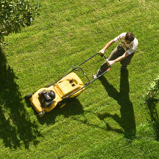 An amber jar soy candle with a black lid, depicted alongside an image of a person mowing a lawn, evoking a suburban atmosphere.